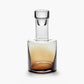 Clear glass decanter with a gradient of brown at the base on a white background