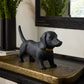 Black dog figurine on a textured surface with plants and a mirror in the background
