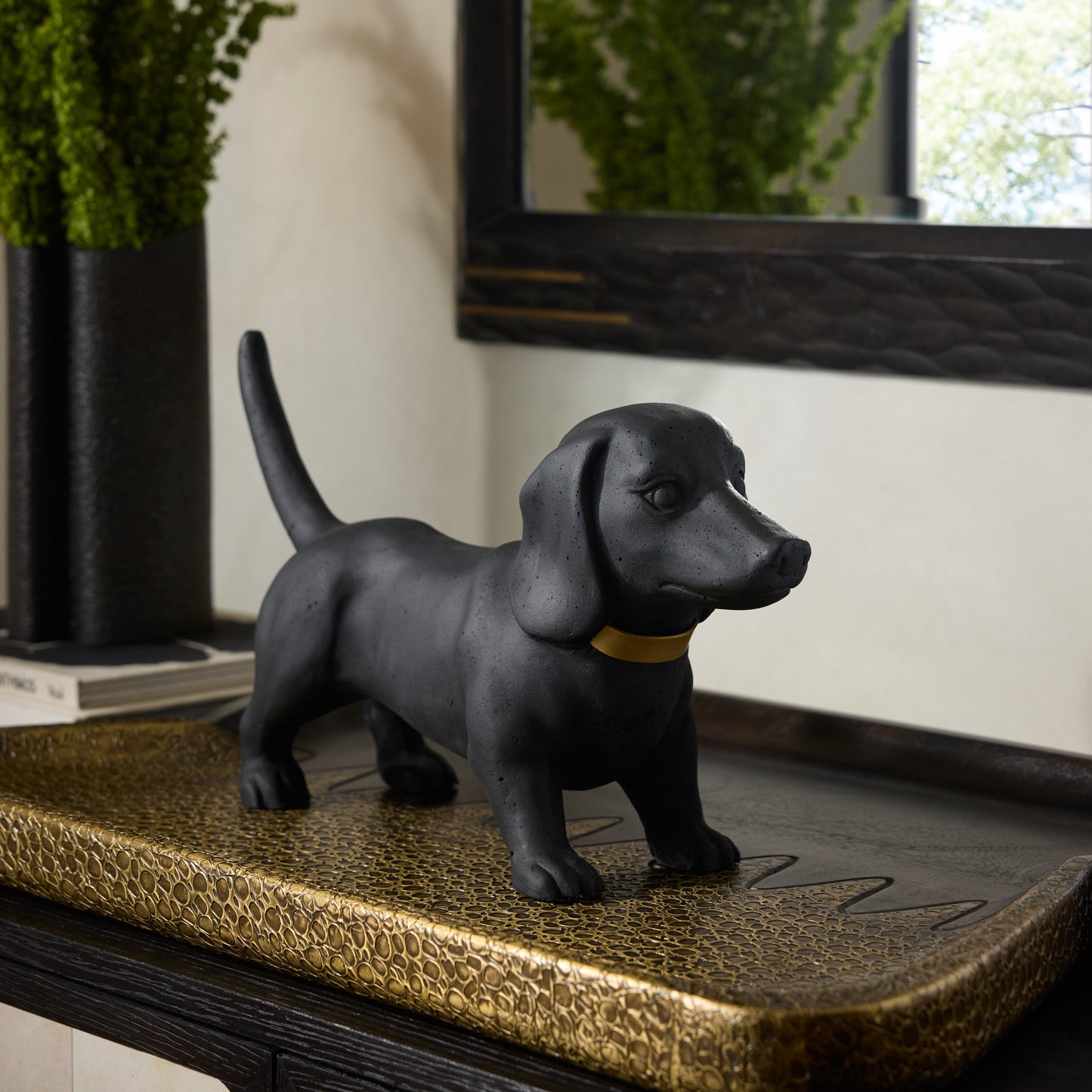 Black dog figurine on a textured surface with plants and a mirror in the background