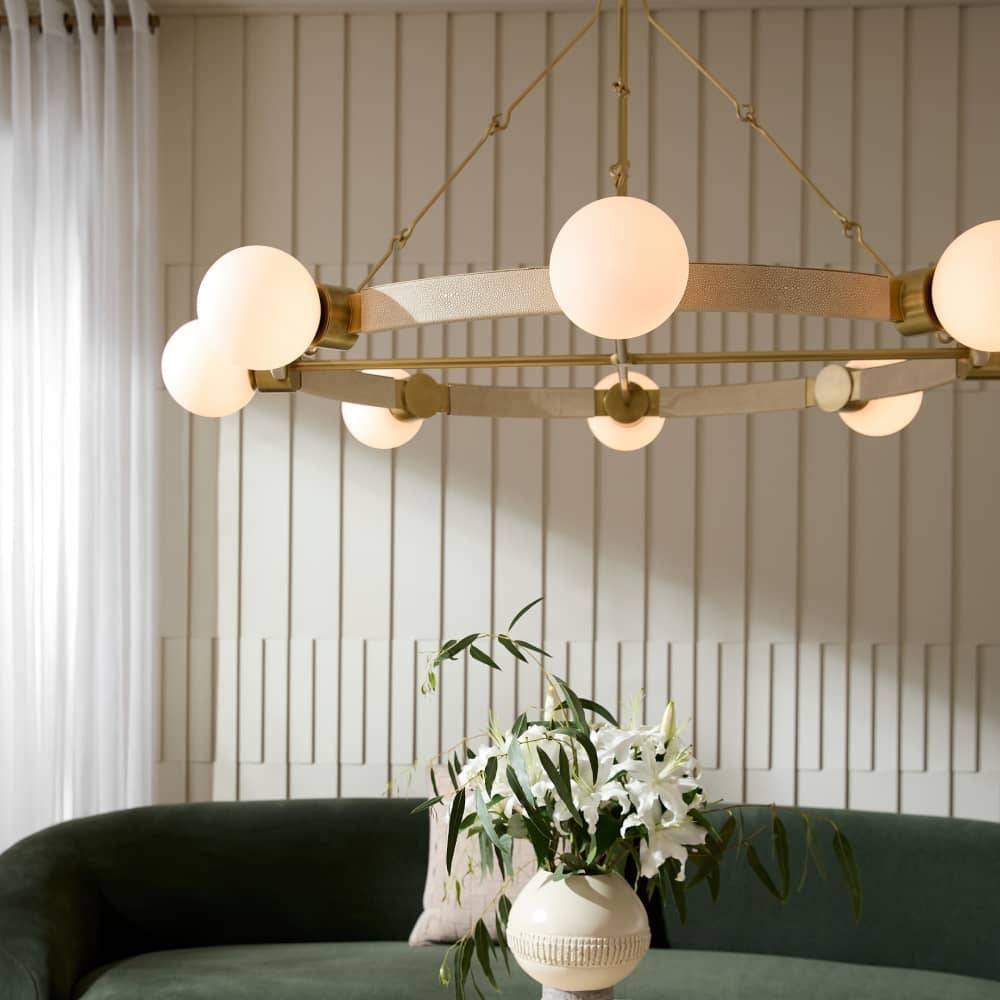 Modern chandelier with spherical lights in a room with a green sofa and white flowers.