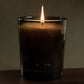 Candle in a glass container with a dark label on a wooden surface and dark background