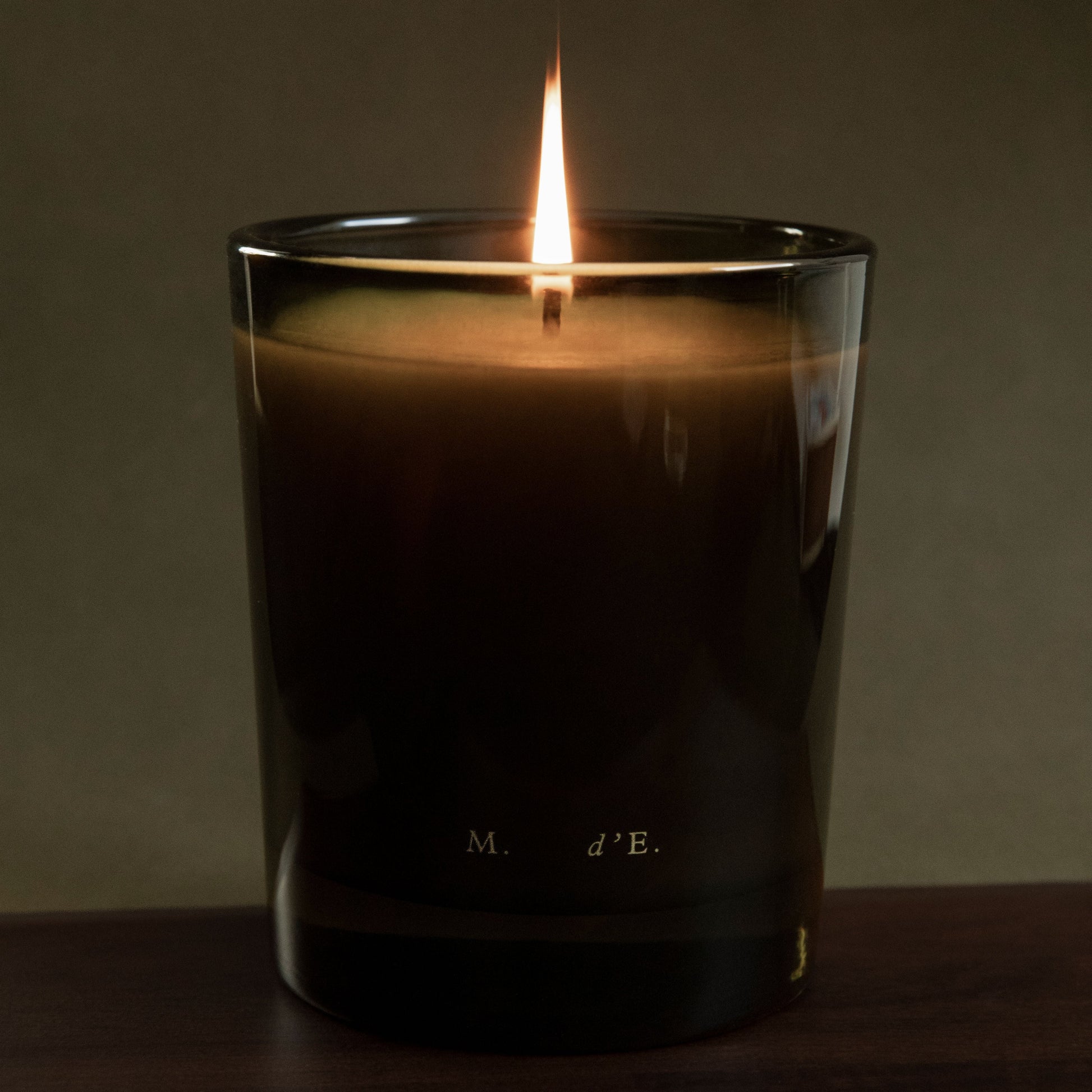 Candle in a glass container with a dark label on a wooden surface and dark background