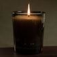 Candle in a glass container with a dark label on a wooden surface and dark background
