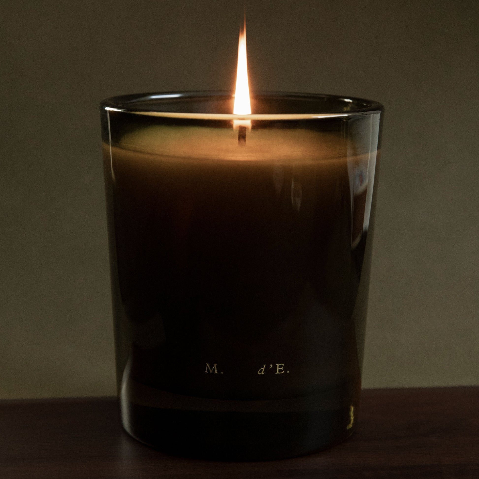 Candle in a glass container with a dark label on a wooden surface and dark background