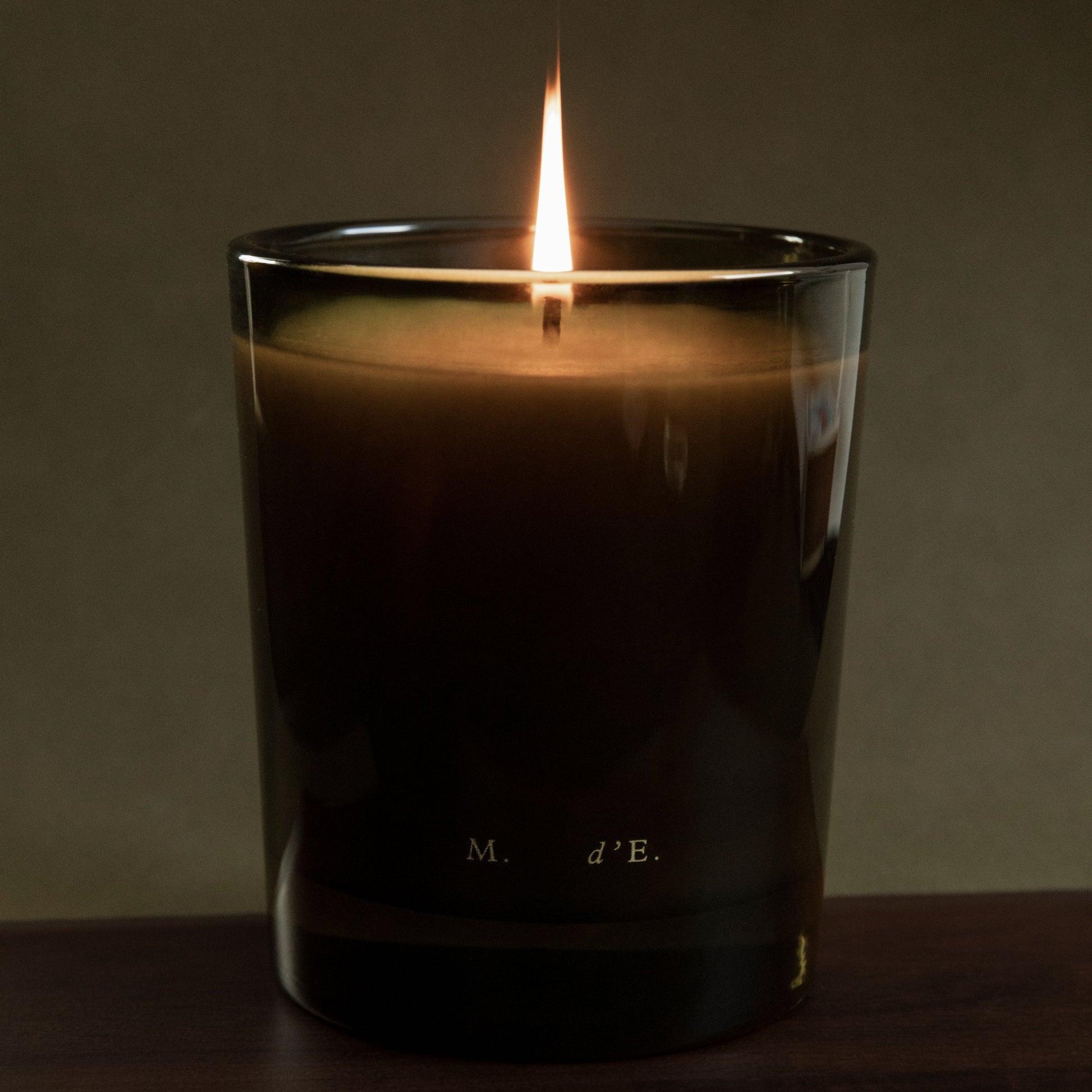 Candle in a glass container with a dark label on a wooden surface and dark background