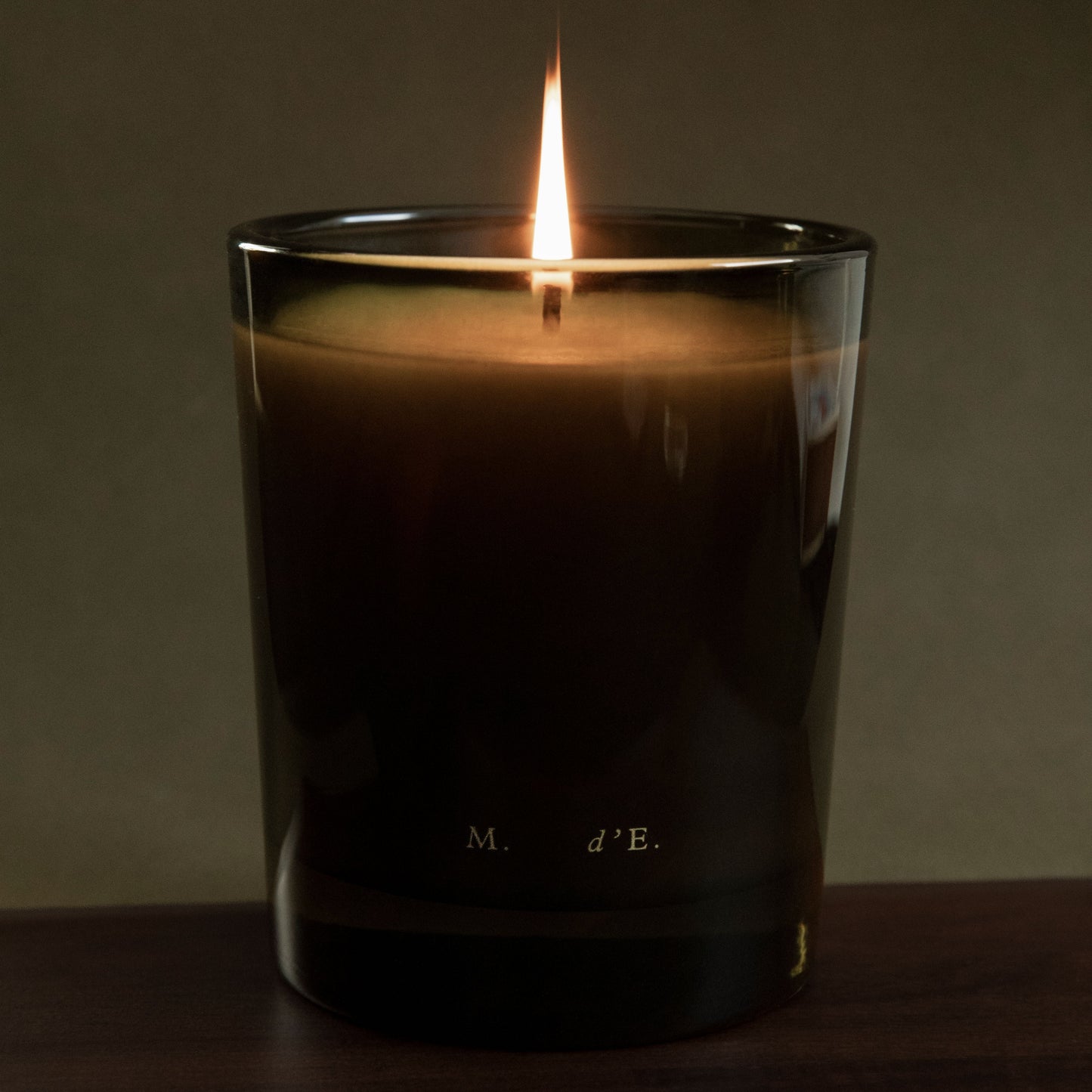 Candle in a glass container with a dark label on a wooden surface and dark background