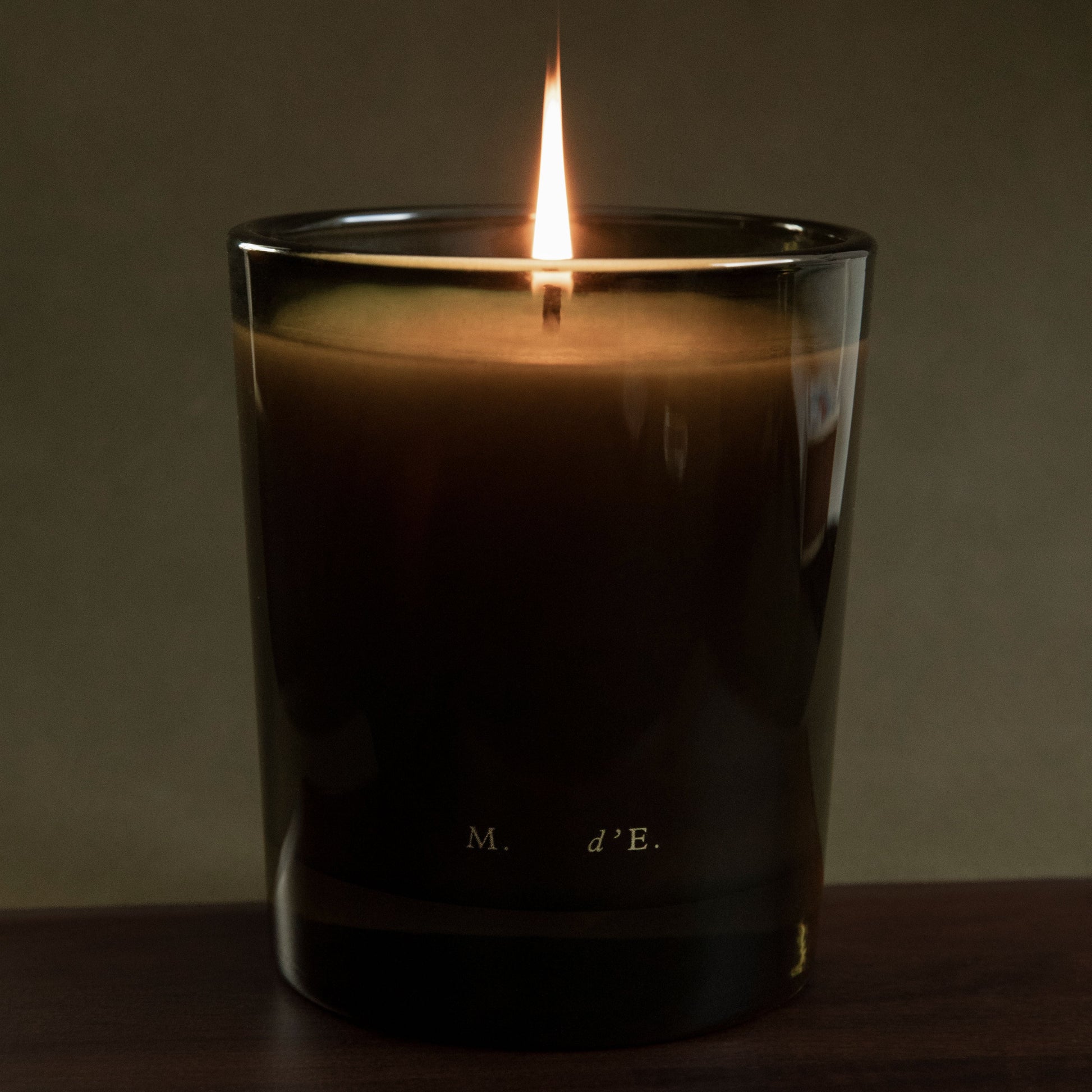 Candle in a glass container with a dark label on a wooden surface and dark background