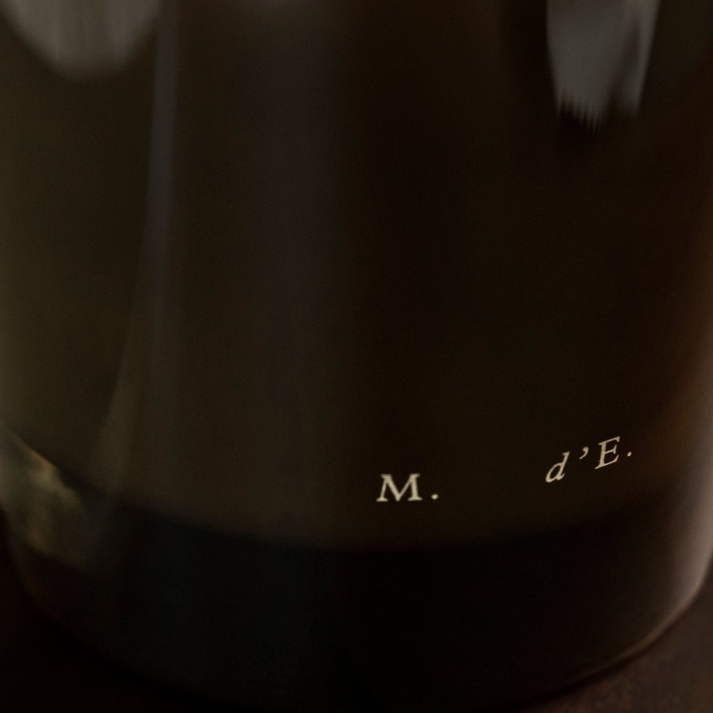 Close-up of a dark fabric with text 'M. d'E.' on a wooden surface