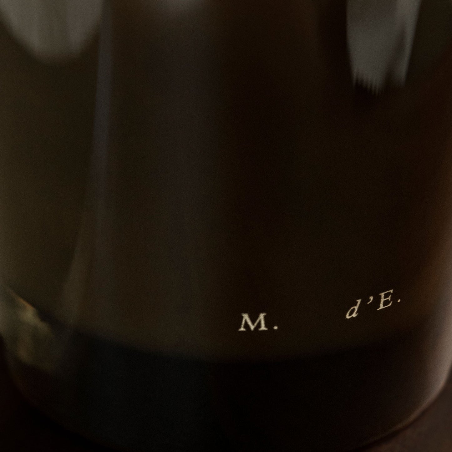 Close-up of a dark fabric with text 'M. d'E.' on a wooden surface