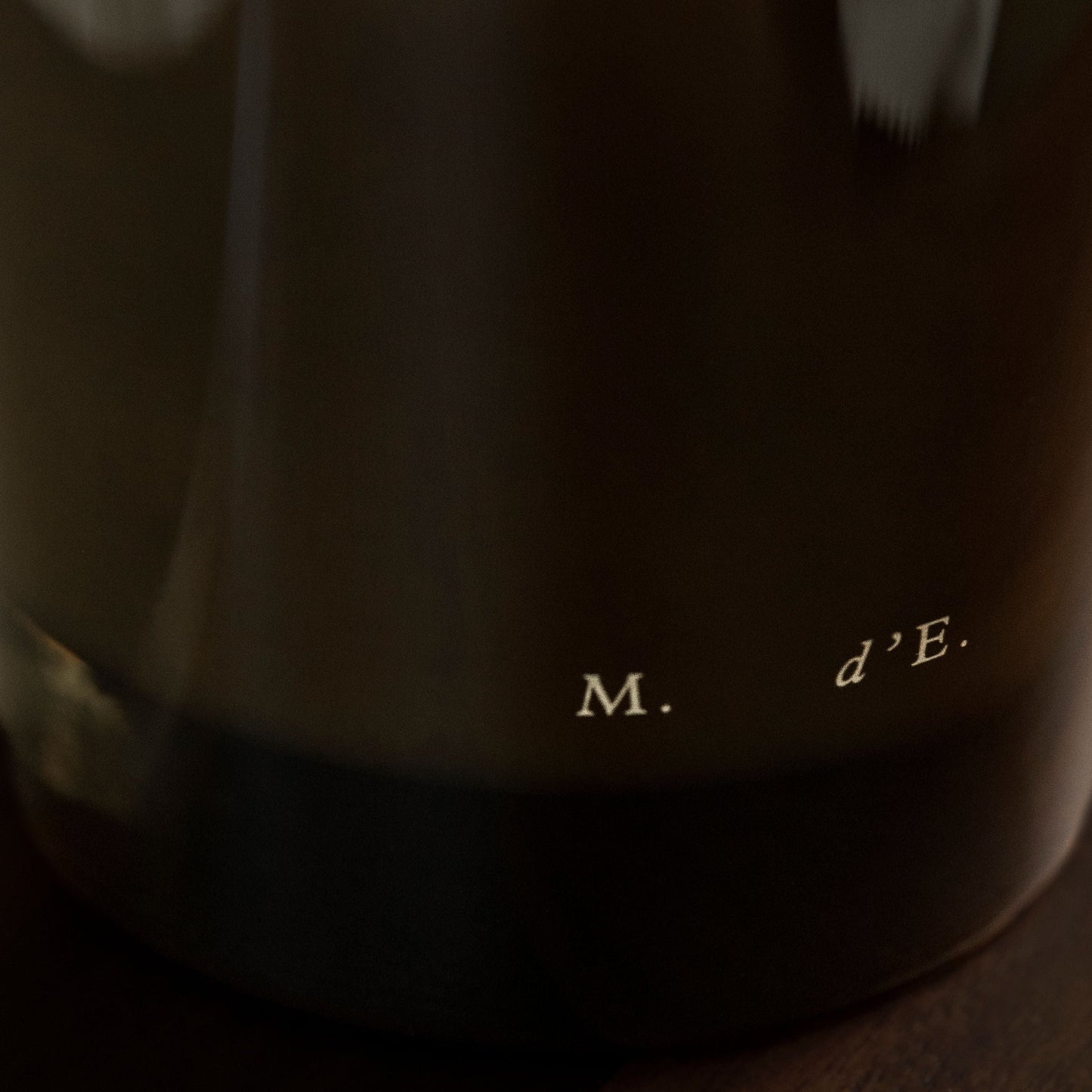 Close-up of a dark fabric with text 'M. d'E.' on a wooden surface