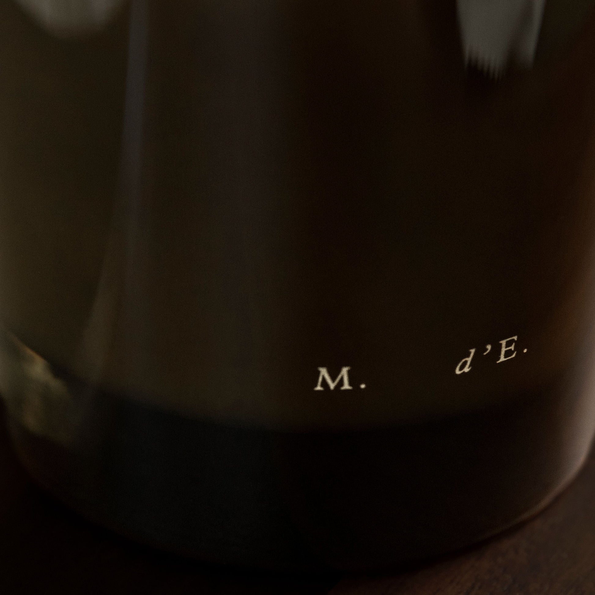 Close-up of a dark fabric with text 'M. d'E.' on a wooden surface