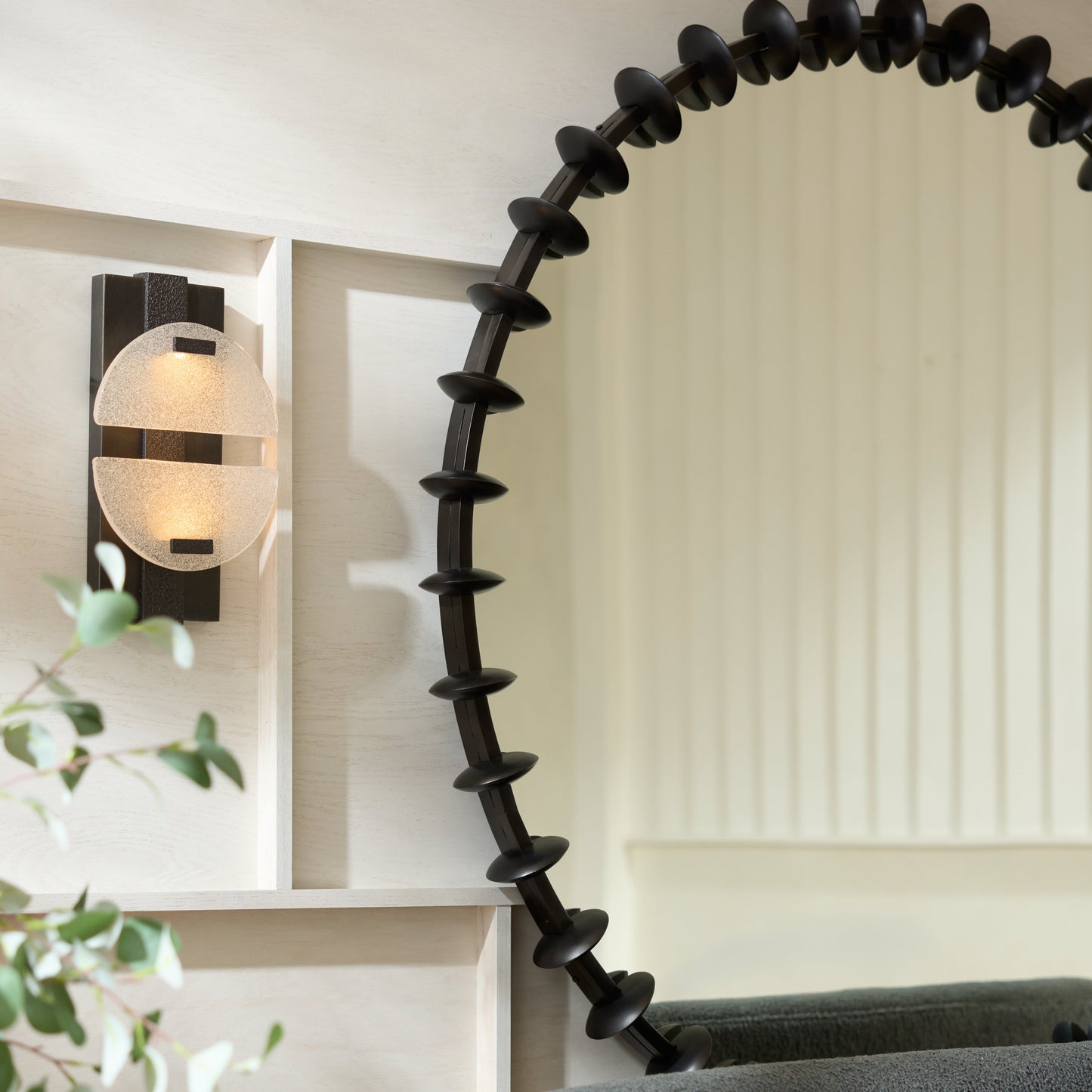 Round black mirror with decorative edge on a gray sofa in a room with a light wall and plant.