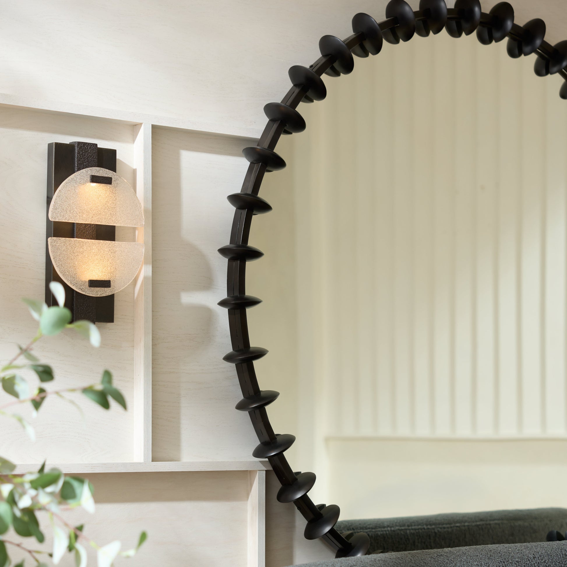 Round black mirror with decorative edge on a gray sofa in a room with a light wall and plant.