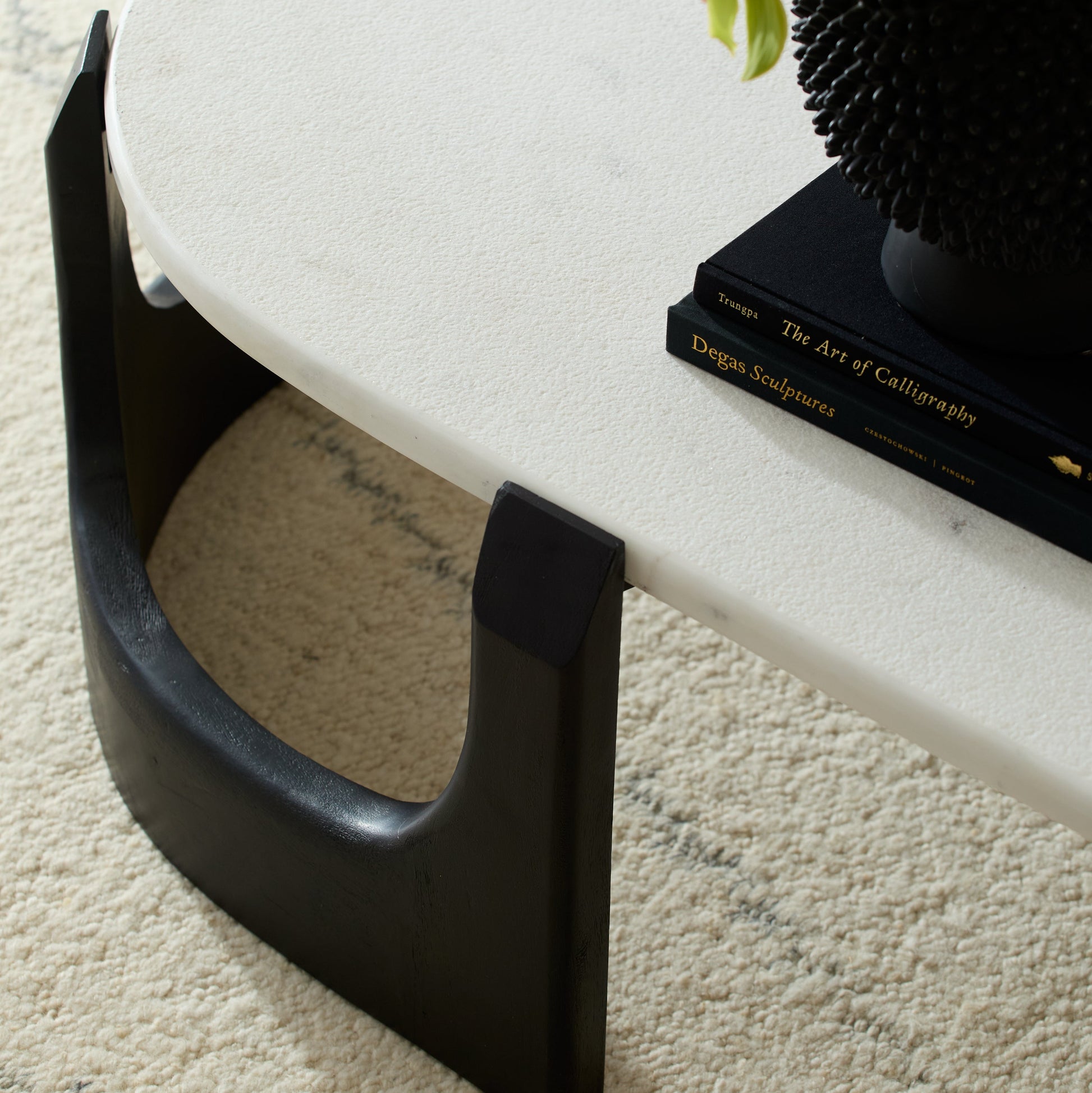 White coffee table with black legs on a beige carpet, featuring a vase of green flowers and a book.