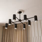 Modern black chandelier hanging against a neutral wall with beige curtains.