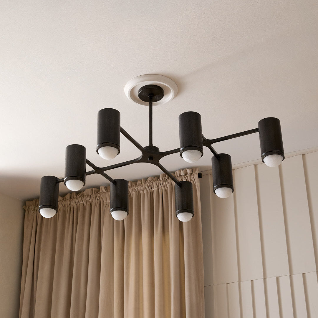 Modern black chandelier hanging against a neutral wall with beige curtains.