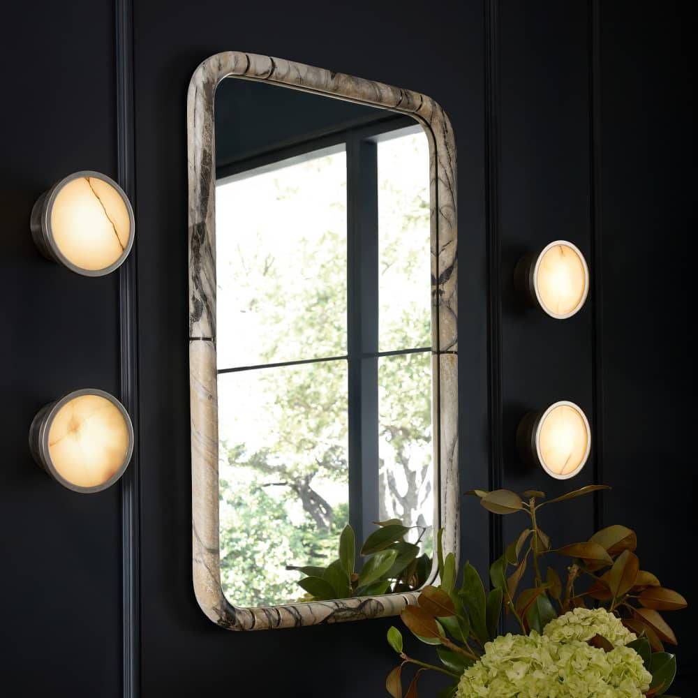 Decorative mirror with marble-like frame and wall lights on a dark wall.