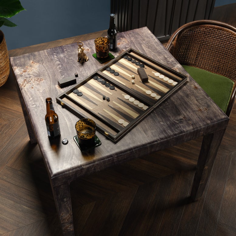 Backgammon board on a rustic wooden table with bottles and glasses.