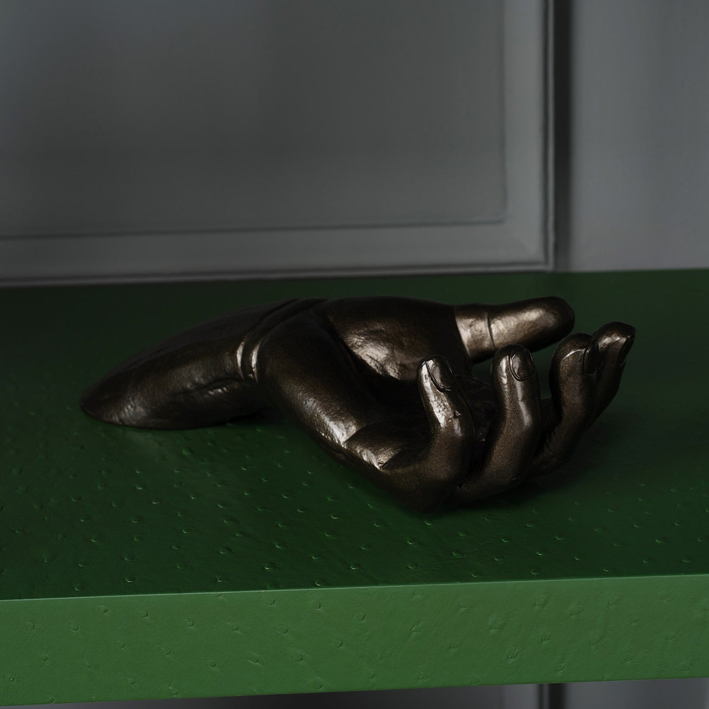 Bronze hand sculpture on a green surface with a neutral background