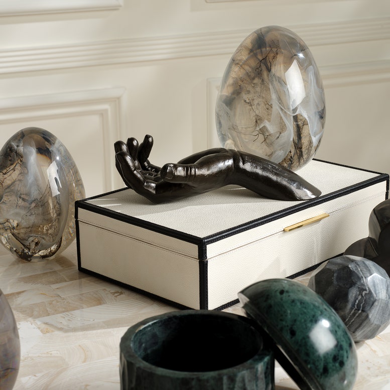 Decorative black sculpture on a white box with marble-like objects in a stylish interior setting.