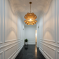 A modern, elegant hallway featuring a distinctive wavy, scalloped white ceiling, white paneled walls, a glowing wavy pendant light, and glossy black marble floor tiles.