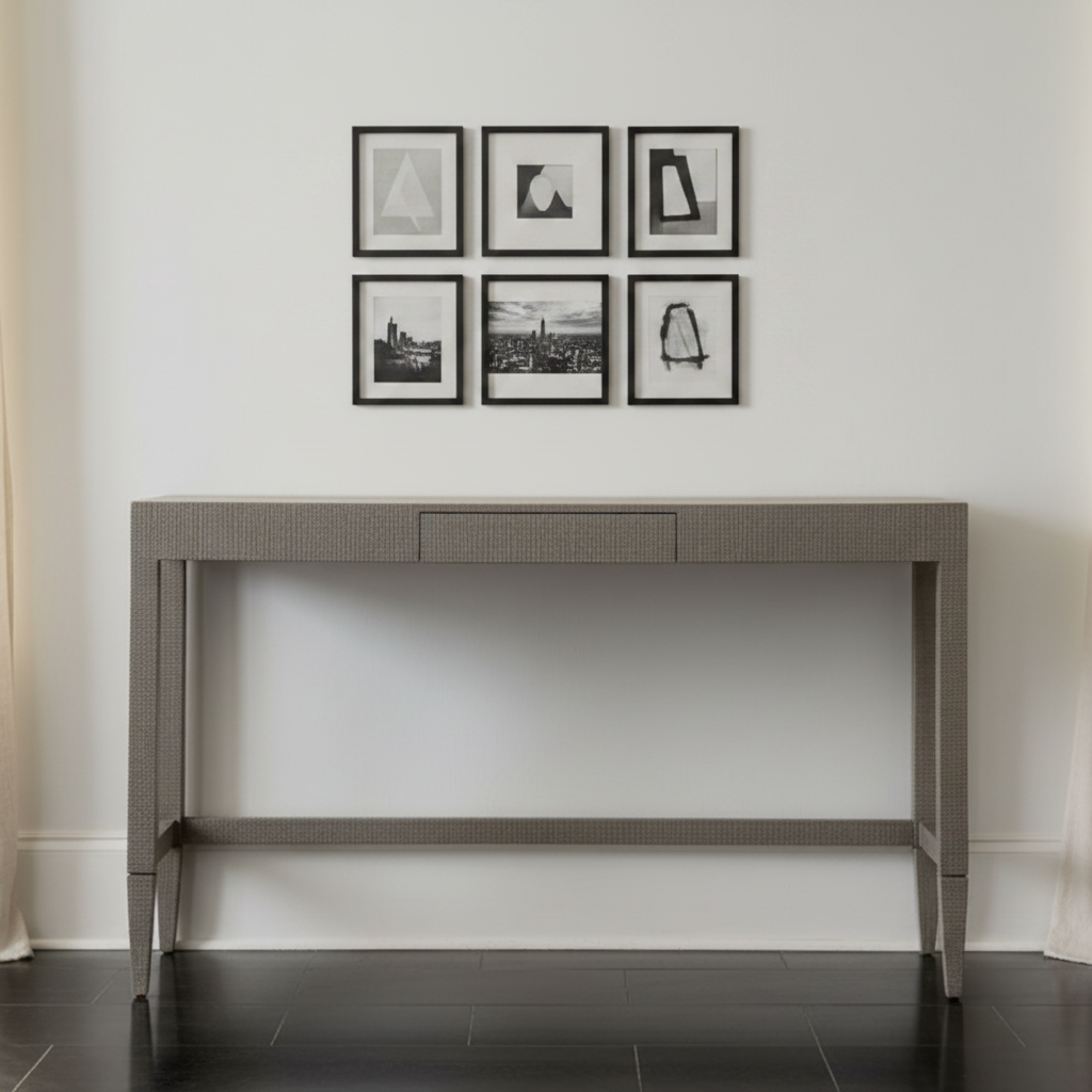 A minimalist gray console table with three drawers and an open lower shelf, set against a white wall with sheer cream curtains and dark reflective flooring.