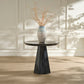 Round black marble table with a textured vase and branches against a light paneled wall.