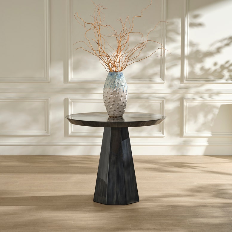 Round black marble table with a textured vase and branches against a light paneled wall.