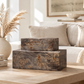 Two stacked rectangular wooden storage boxes with a dark weathered finish and natural wood grain, displayed on a light wood table in a cozy living room setting.