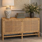 A mid-century modern sideboard cabinet made of natural woven rattan, styled with a ceramic table lamp, stacked boxes, and a floral arrangement on top.