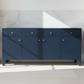 A navy blue wooden sideboard with six drawers and doors, accented by small round brass handles, set against a white marble wall with dramatic diagonal sunlight shadows.