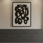 A dark gray sideboard cabinet in a styled room, decorated with a vase of pampas grass, books, a gold table lamp, and a large black and white abstract framed print on the wall above it.