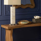Wooden console table with a lamp and decorative items against a dark blue wall.