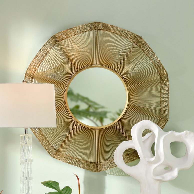 Decorative wall mirror with gold frame on a light green wall.