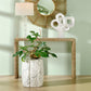 Decorative table with a plant, vase, and abstract sculpture against a light green wall.