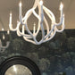 Two white chandeliers hanging above a round mirror with a dark frame against a decorative wall.