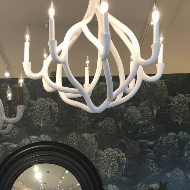 Two white chandeliers hanging above a round mirror with a dark frame against a decorative wall.