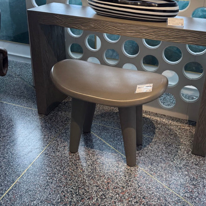 Small wooden stool with a round seat in front of a decorative wall with circular cutouts.