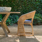 Wicker chair with a cushion next to a wooden table outdoors.