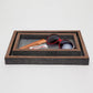 Decorative tray with sunglasses, comb, and tube of lip balm on a light gray background