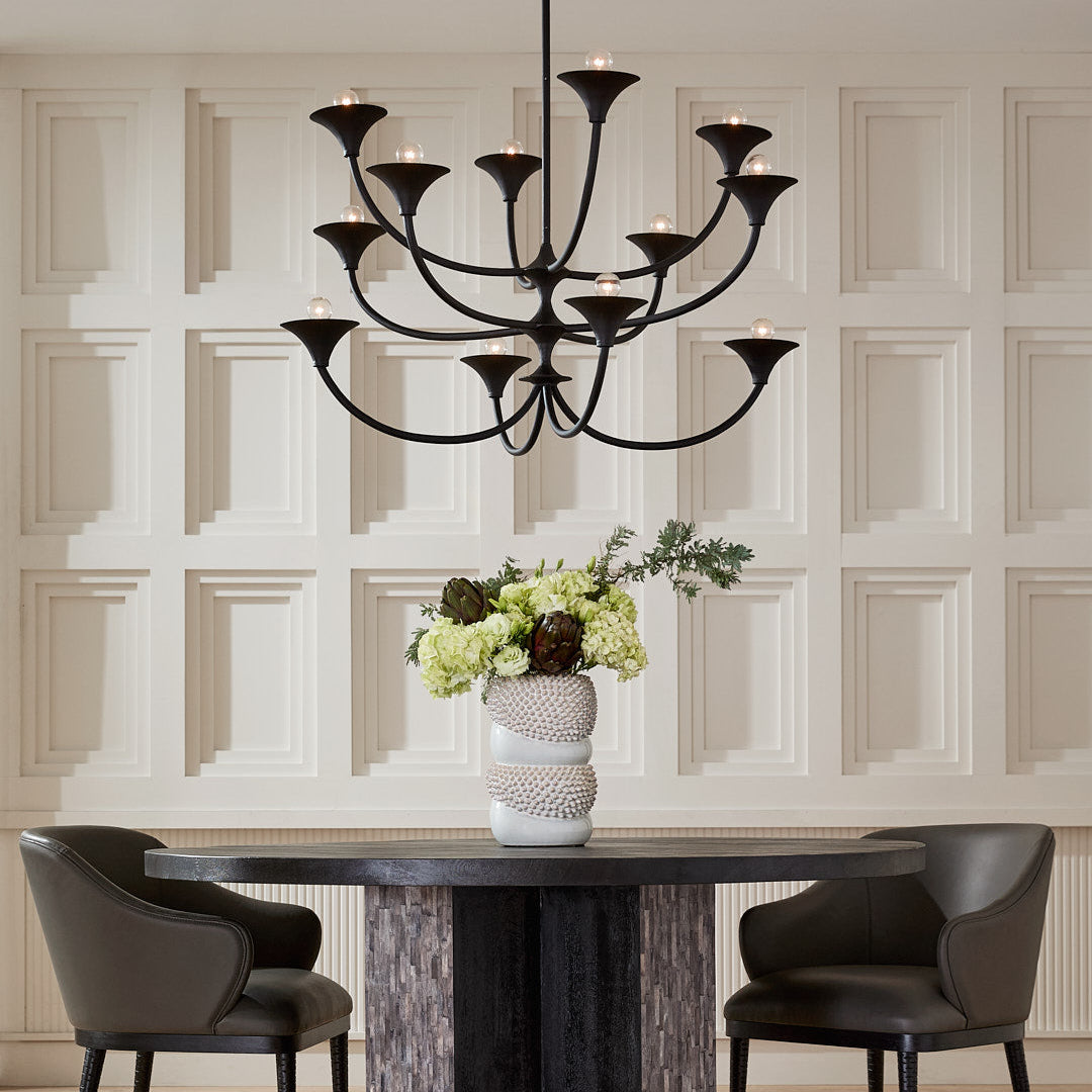 Dining room with a black chandelier, round table, and chairs against a paneled wall.