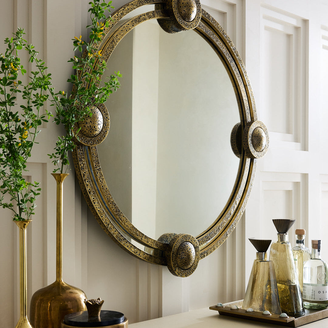 Decorative round mirror with gold accents on a wall above a cabinet with decorative items.