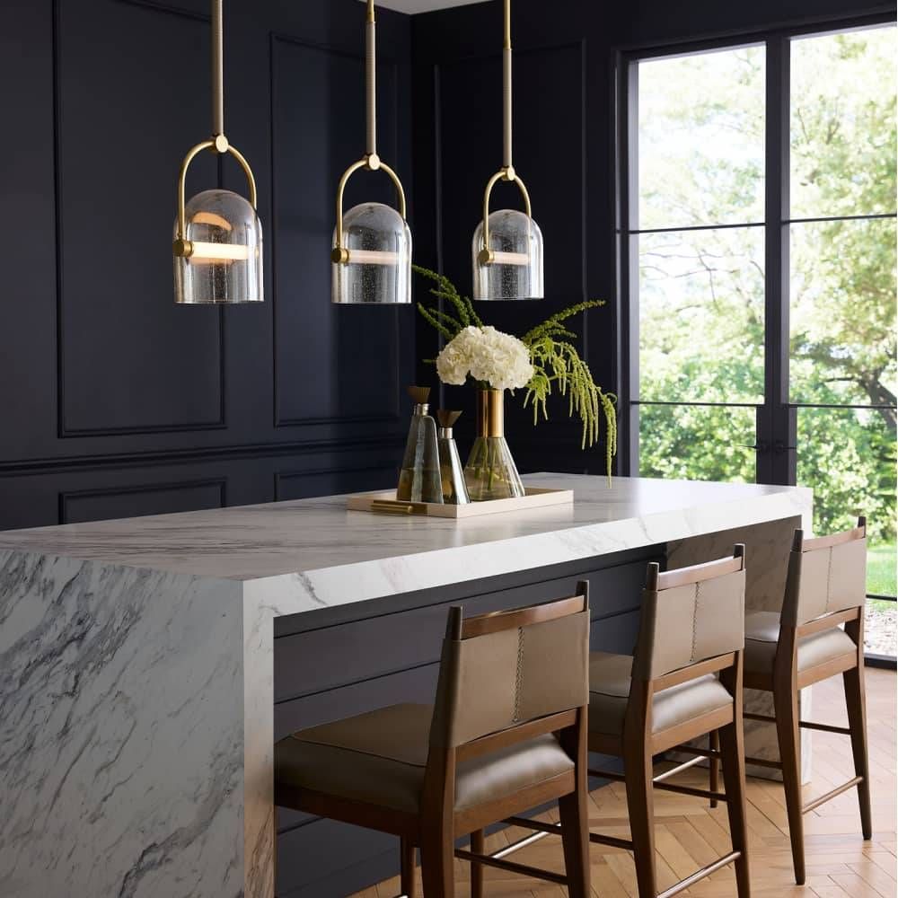 Modern kitchen island with marble countertop, pendant lights, and chairs.