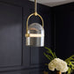 Pendant light fixture with clear glass shade and gold accents against a dark wall.
