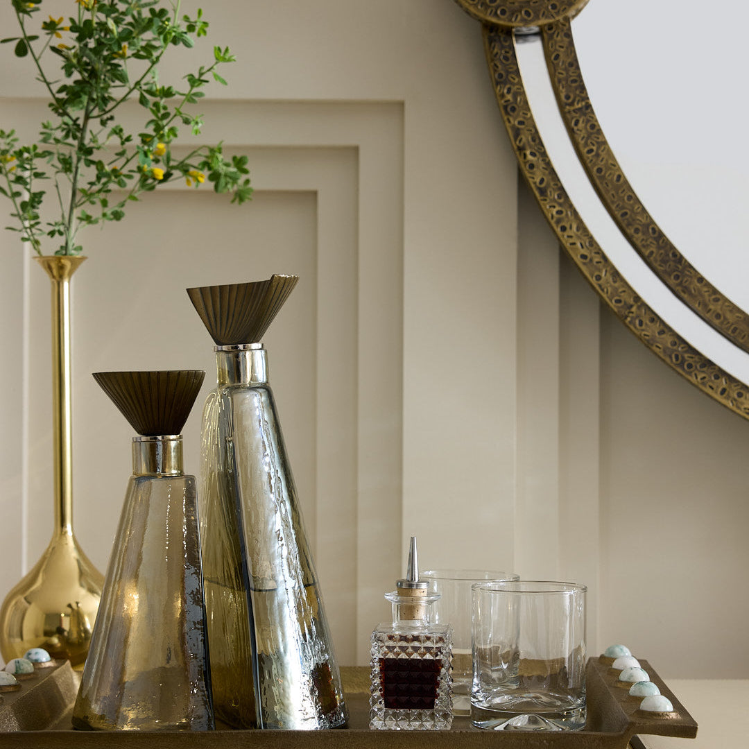Decorative tray with glassware and vases on a shelf, featuring a decorative mirror in the background.