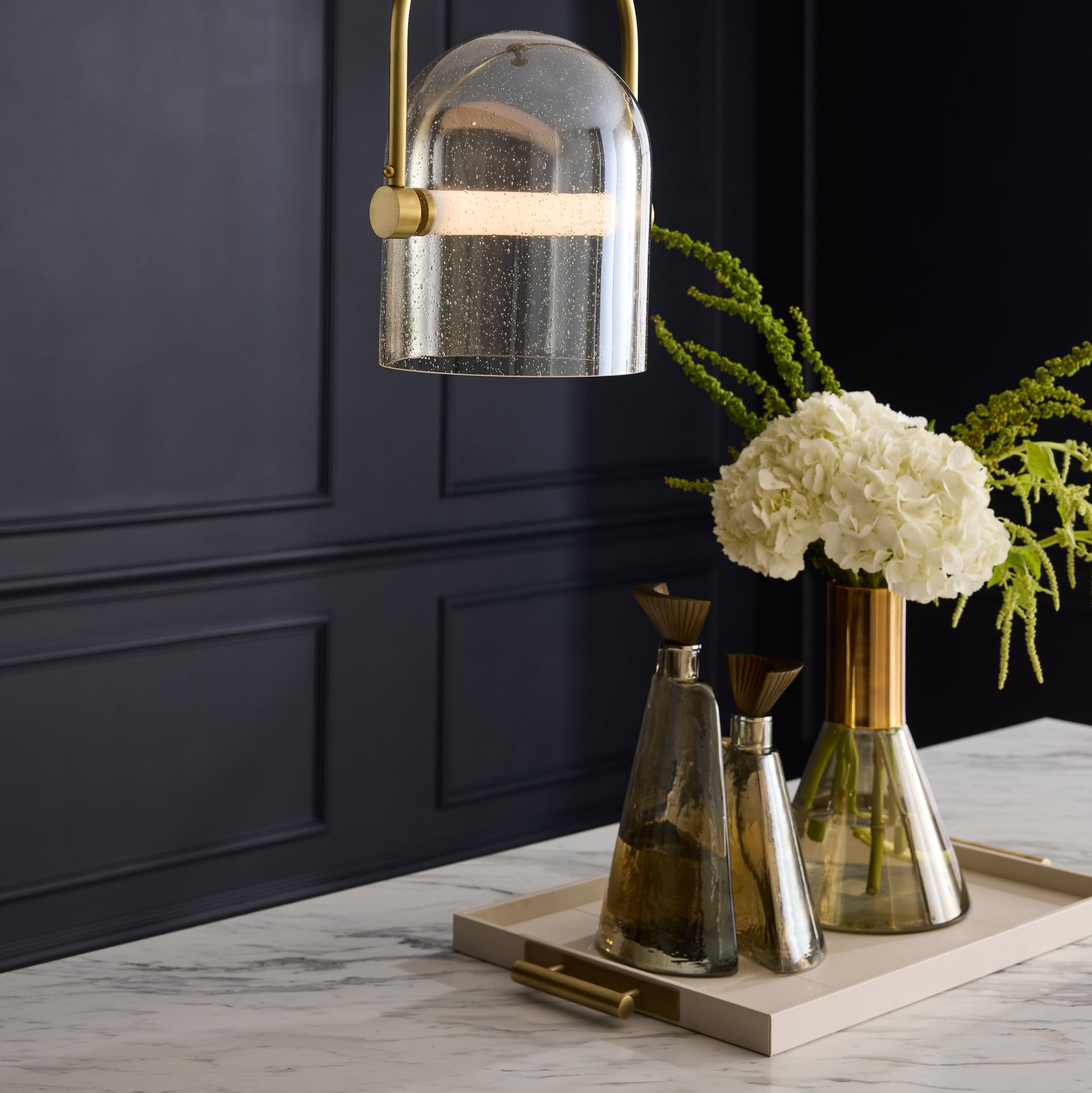 Decorative pendant light fixture with floral arrangement on a marble surface against a dark paneled wall.