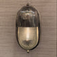 A vintage oval wall sconce with a polished silver metal frame and a ribbed clear glass shade, shown against a textured gray wall.