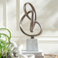 Decorative metal sculpture on a marble base with a plant and books in the background