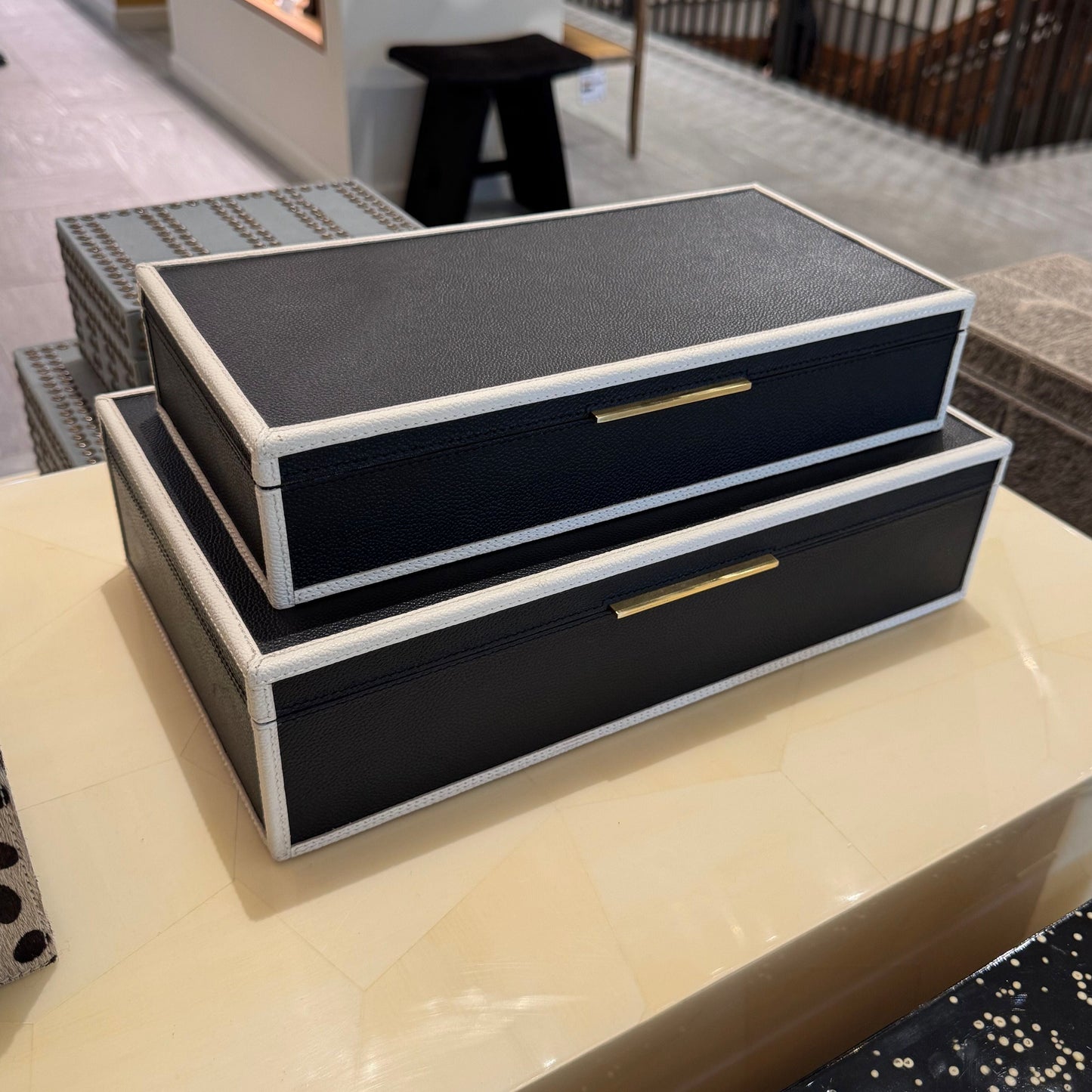 Two black jewelry boxes with gold accents on a counter in a store setting.