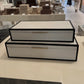 Two black and white jewelry boxes on a table with a store interior in the background.